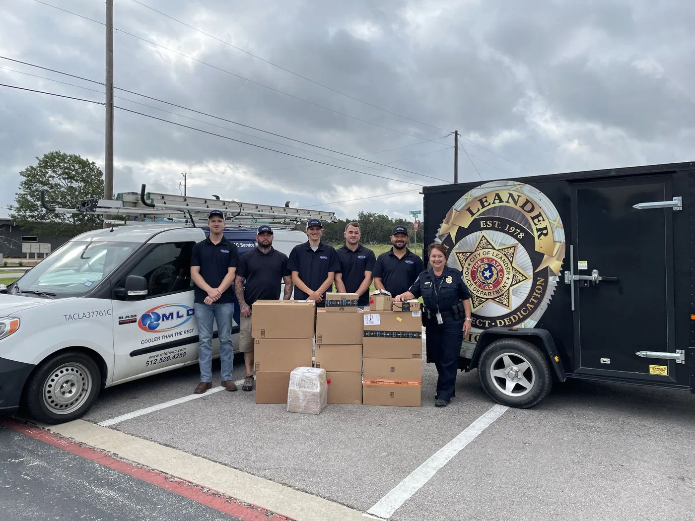 The MLD Services team with a Leander Police Department officer beside a company van and LPD trailer during a donation drop-off.